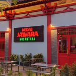 Muka gerai Kedai Jawara Nusantara di Park Shanghai Pakuwon City Surabaya dengan papan neon dan meja teras menjelang malam