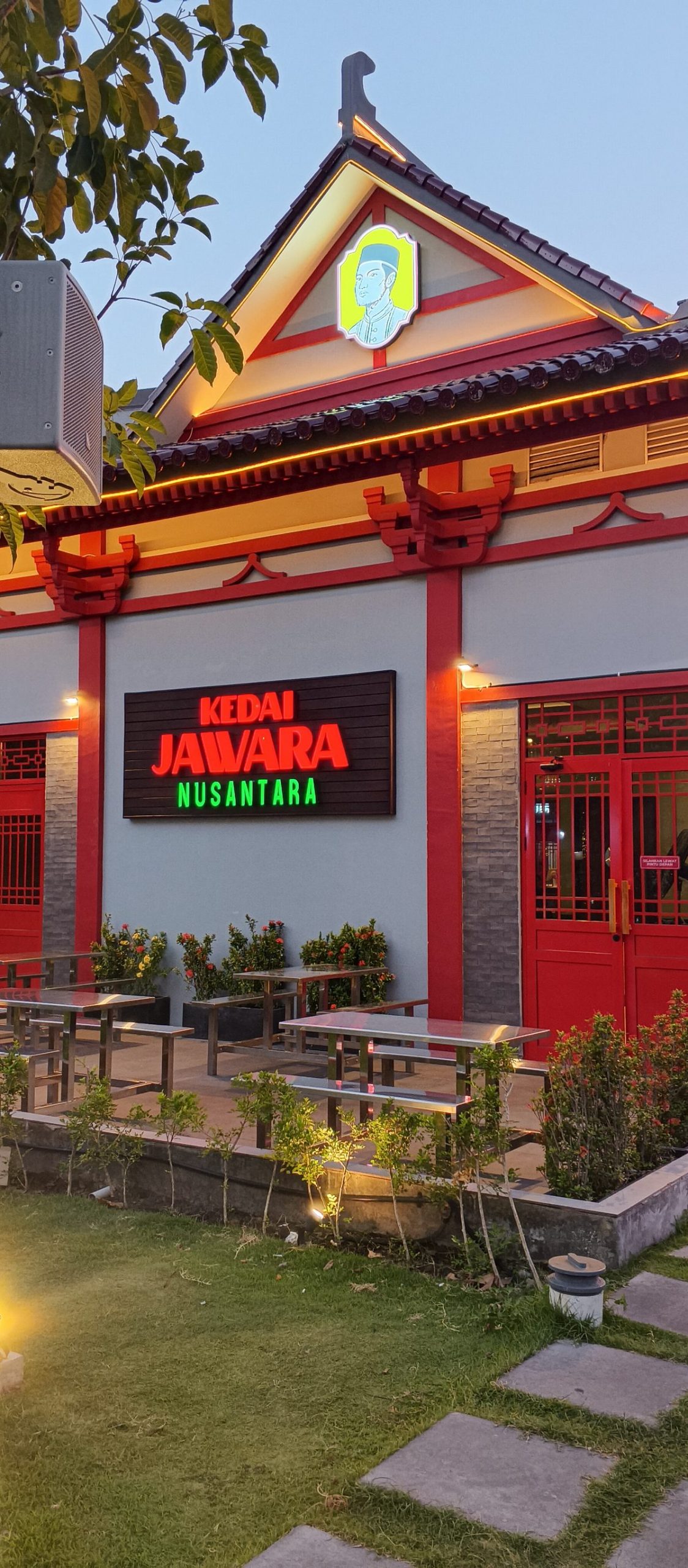 Muka gerai Kedai Jawara Nusantara di Park Shanghai Pakuwon City Surabaya dengan papan neon dan meja teras menjelang malam